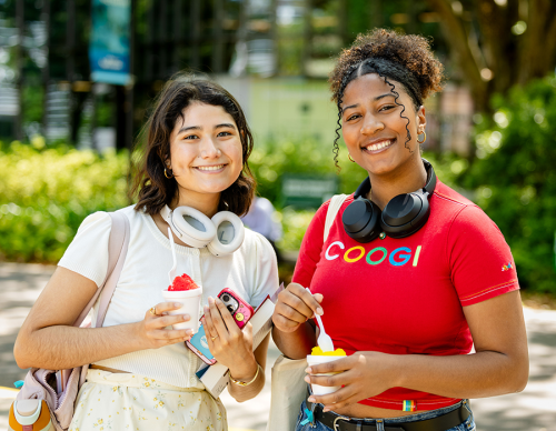 Summer School Two students smiling at the camera with headphones around their necks and cups of snowballs.
